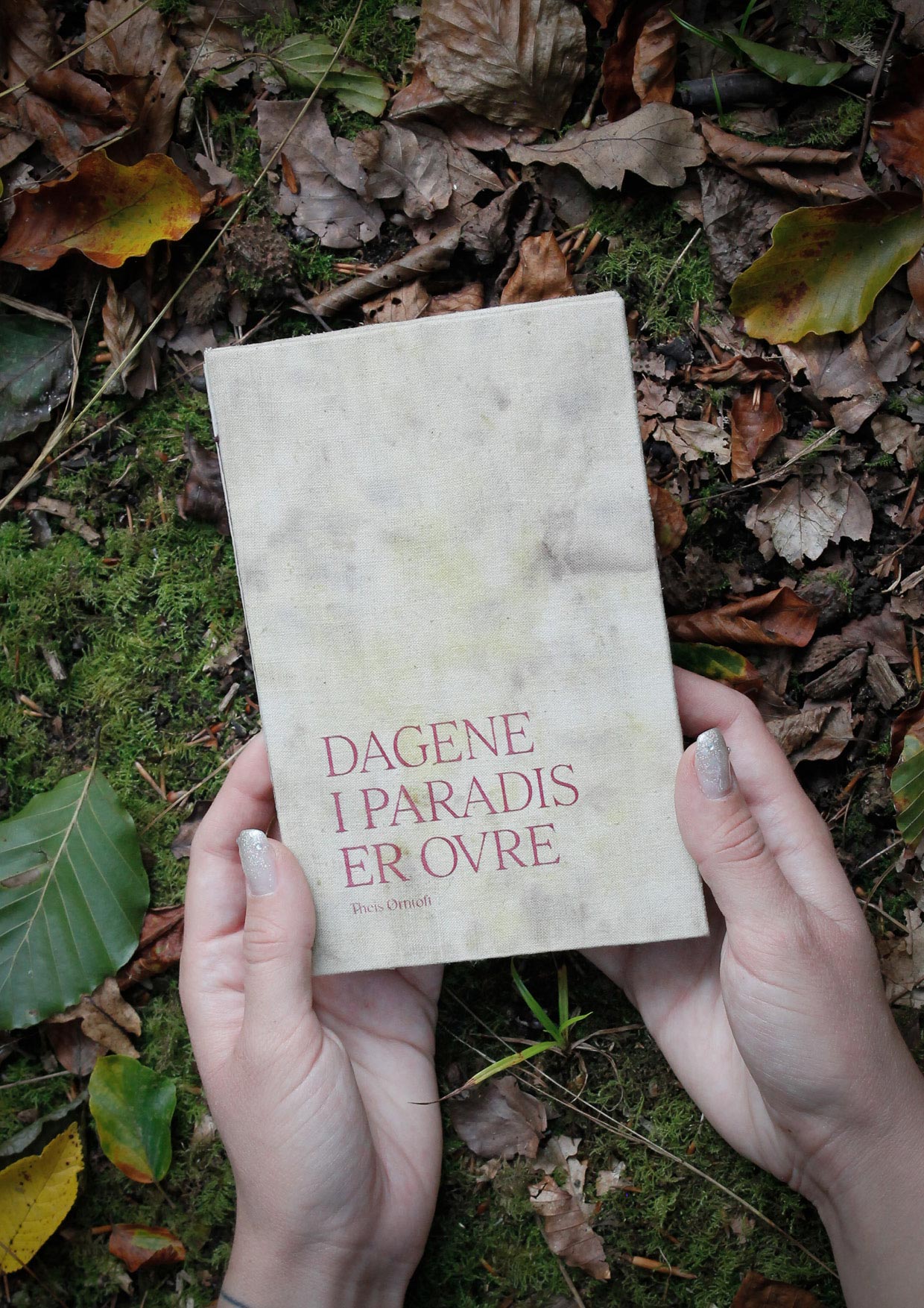 Two hands holding a book bound in handdyed fabric in the forest.