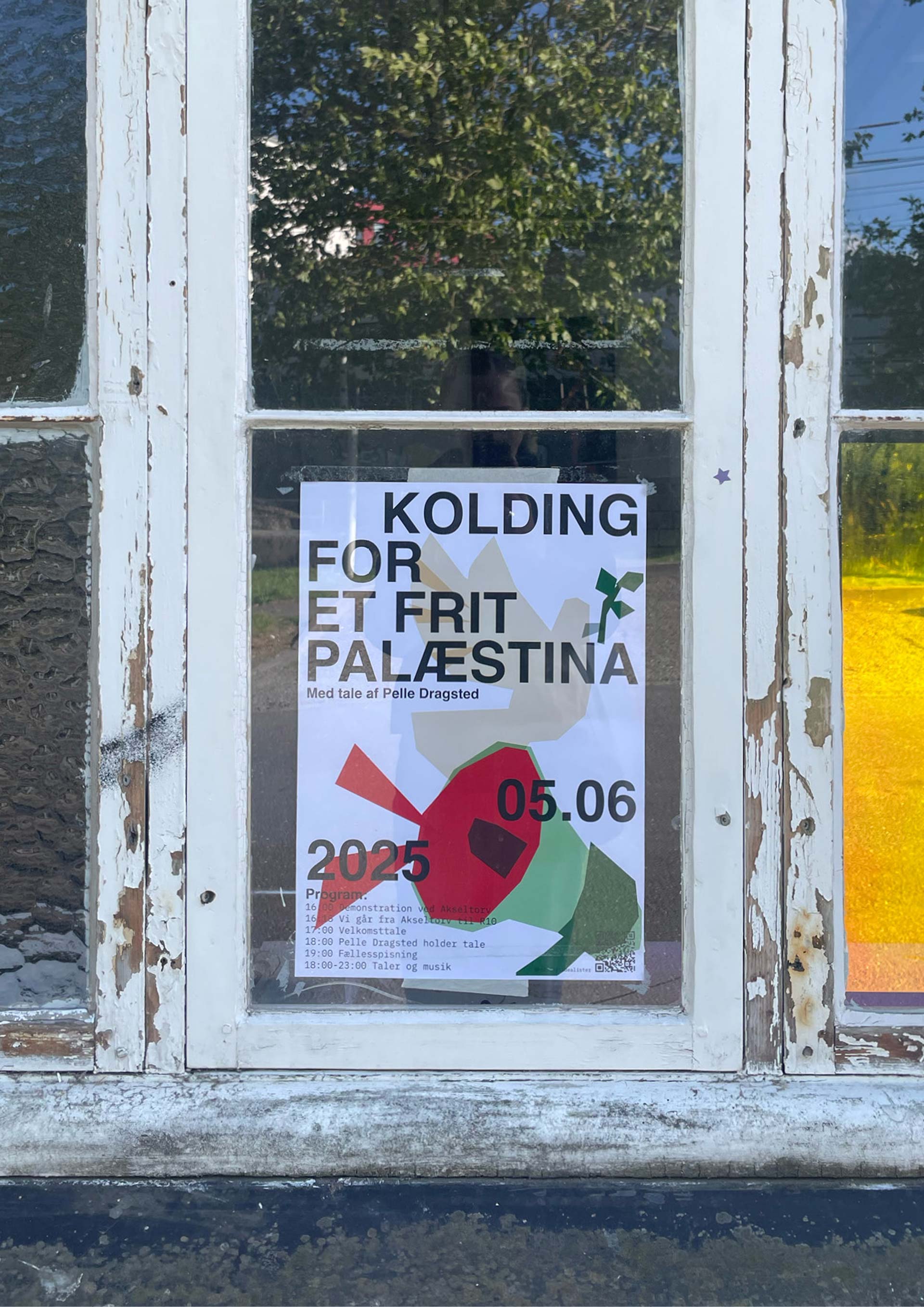 Black/green/red/white eventposter hanging in a window.