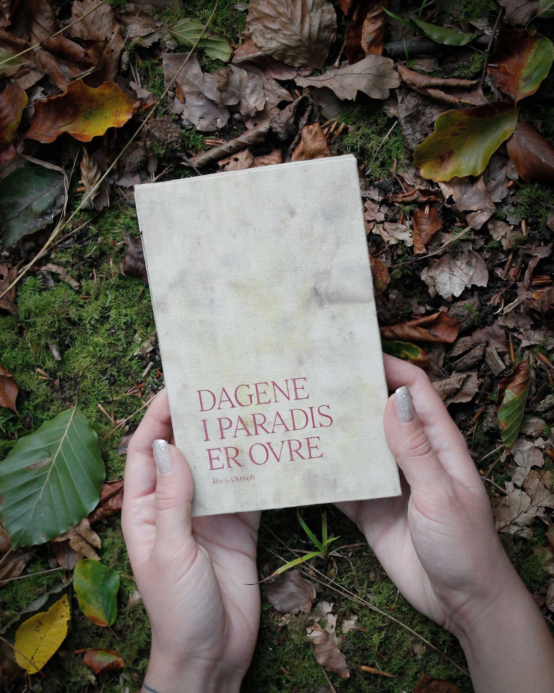 Two hands holding a book with handdyed fabric in the forest.