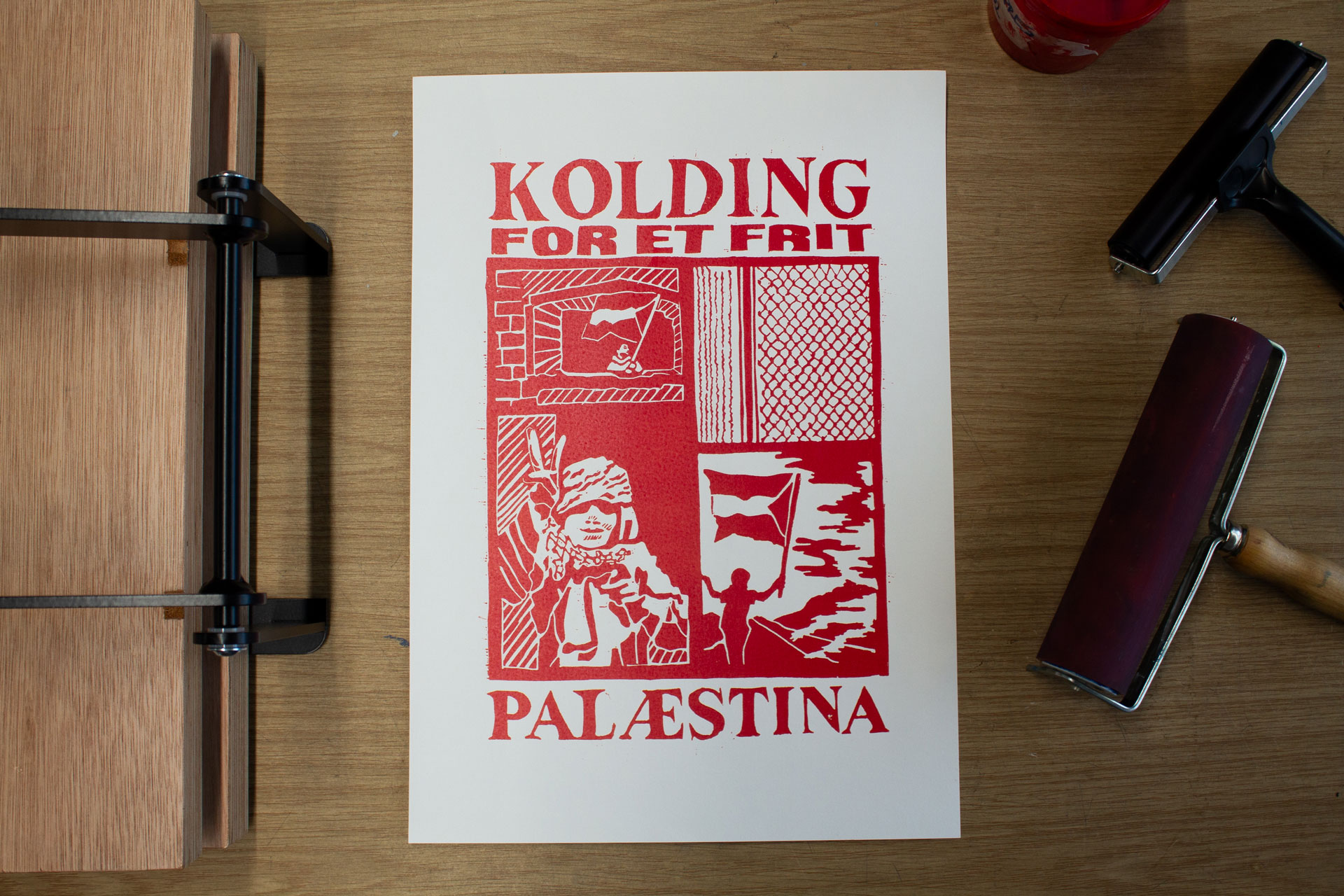 Red linocut on white paper lying on a wooden table surrounded by tools.