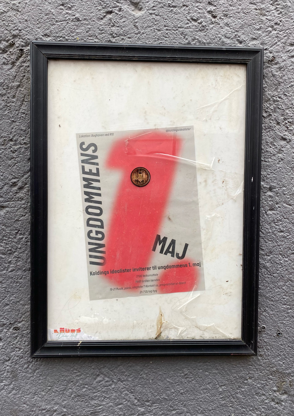 Eventposter hanging within a frame on an outside wall.