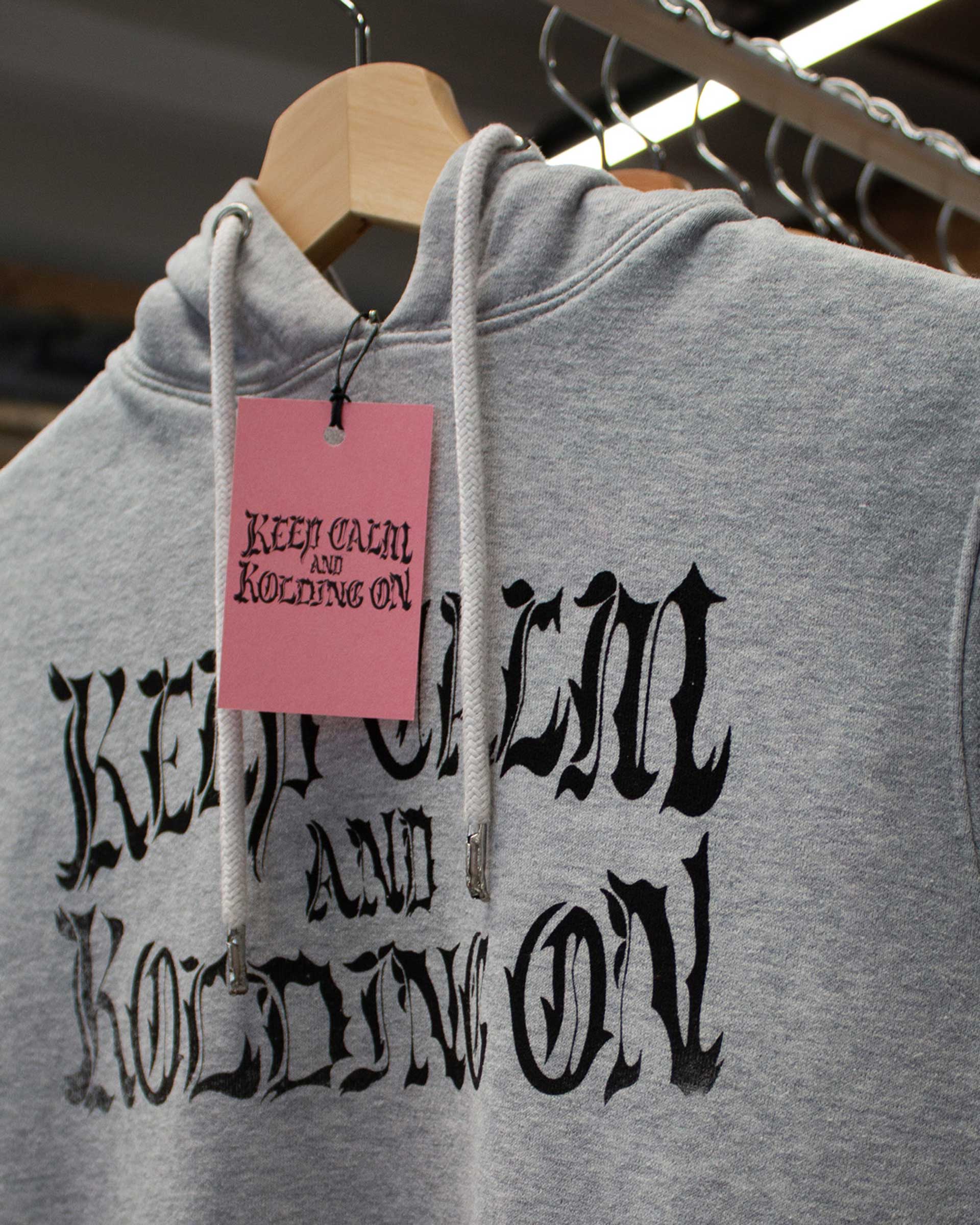 A grey hoodie with black print and a pink necklabel.